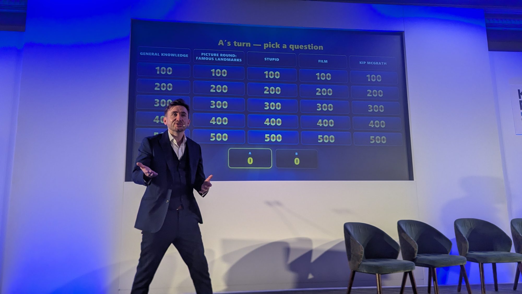 Kevin Durham hosting a company conference with a live quiz show board on the big screen behind him