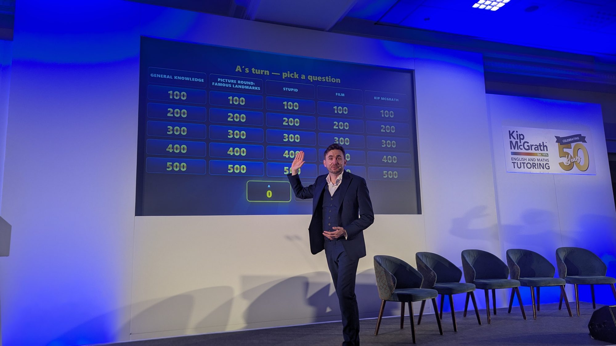 Kevin Durham on the conference stage introducing a whole-room game on the big screen