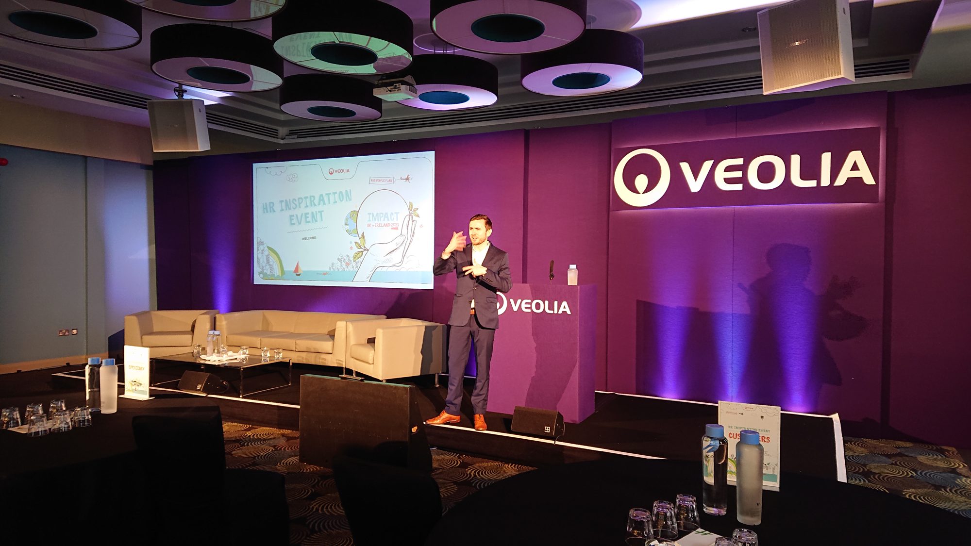 Kevin Durham hosting an HR event on a wide stage, with round tables set for delegates